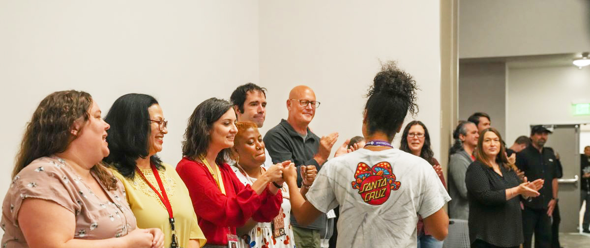 A row of employees applaud for a student