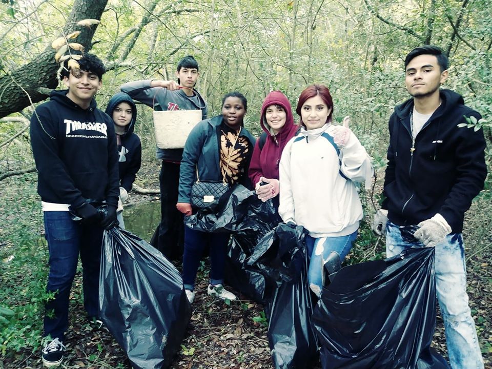 Seven students pick up trash in a wooded area