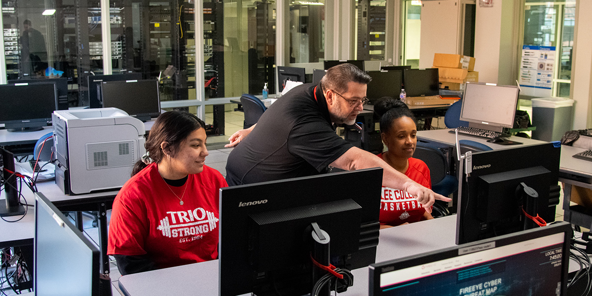 An instructor points to something on a computer screen as students watch