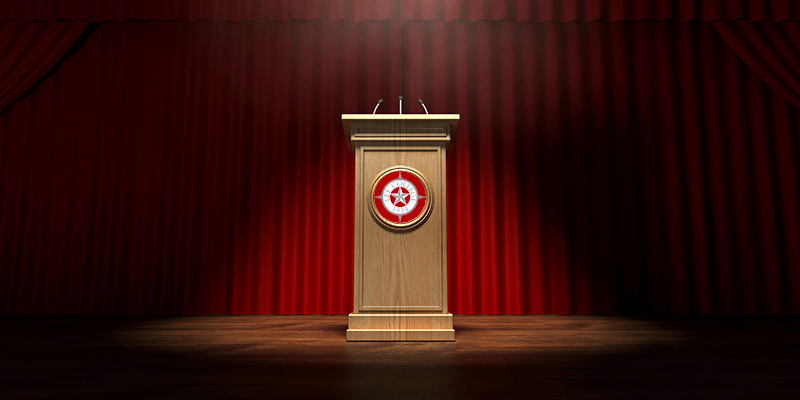 A lectern on a stage with red curtains behind