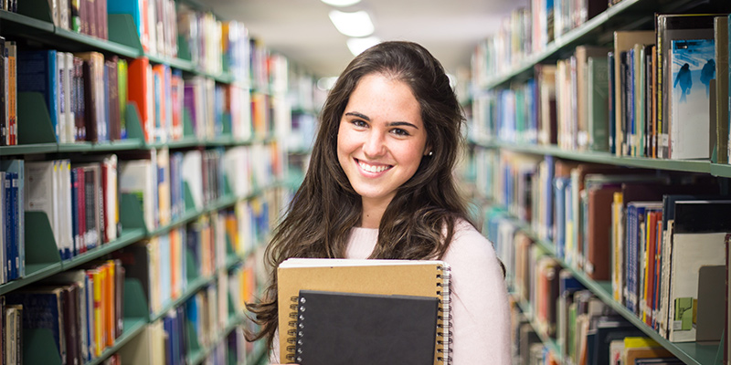 A smiling female student holding notebooks in a library