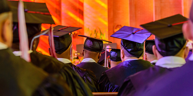 Inmates in caps and gowns at their graduation ceremony (seen from behind)