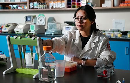 A student in a white coat works in a lab