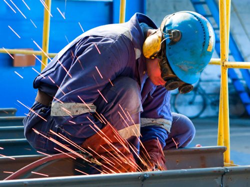 A worker in goggles and a hard hat, with sparks flying.